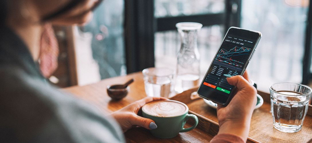 A woman look at a coffee shop looking at the stock market on her phone.