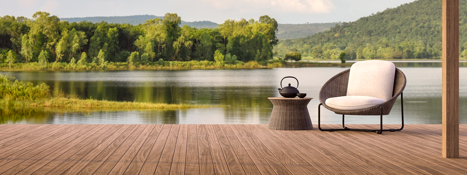 A wicker armchair on a dock by a gorgeous lake surrounded by trees.
