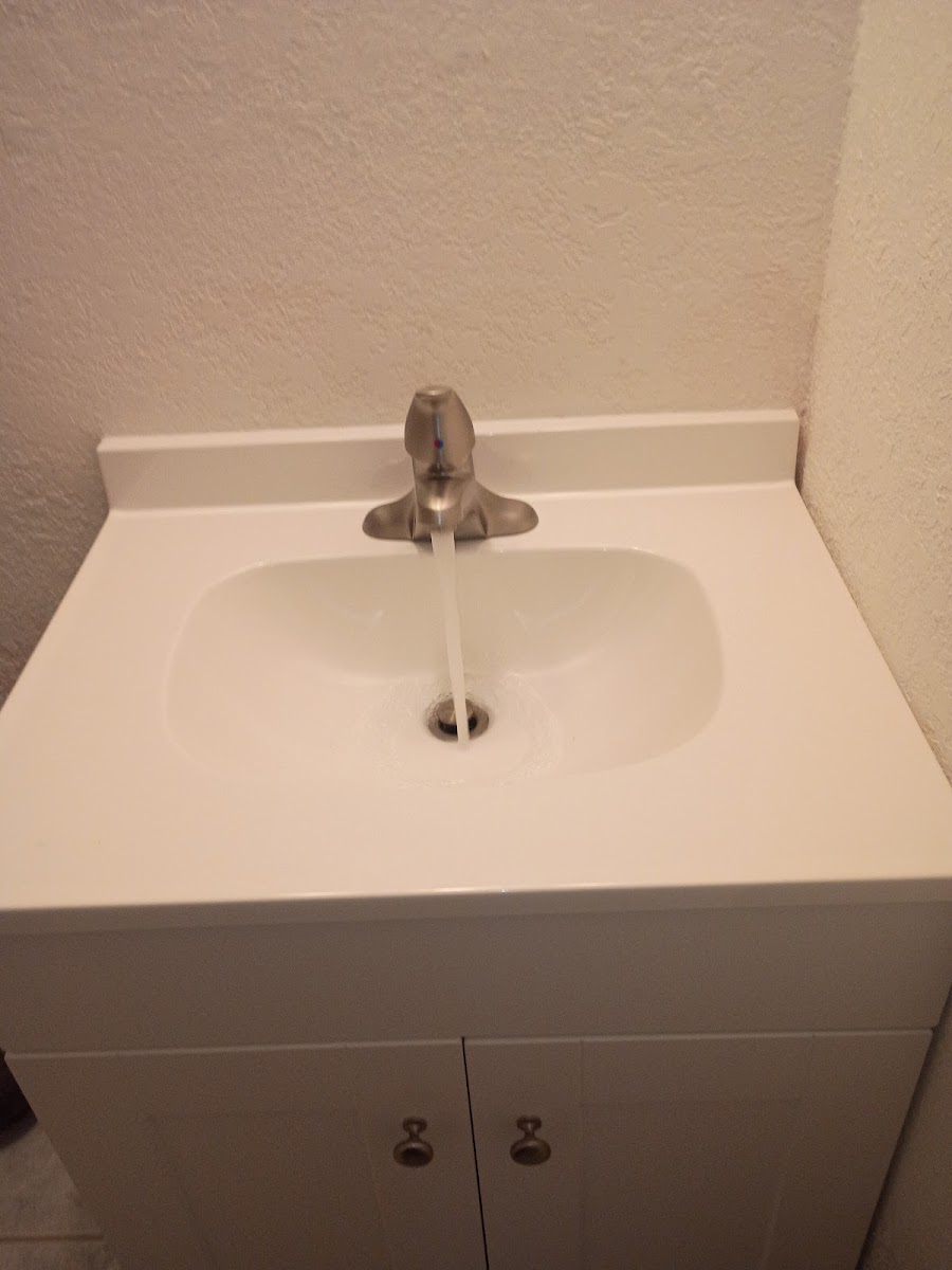 Bathroom vanity sink with faucet and cabinet, showcasing a clean plumbing fixture installation or repair area.