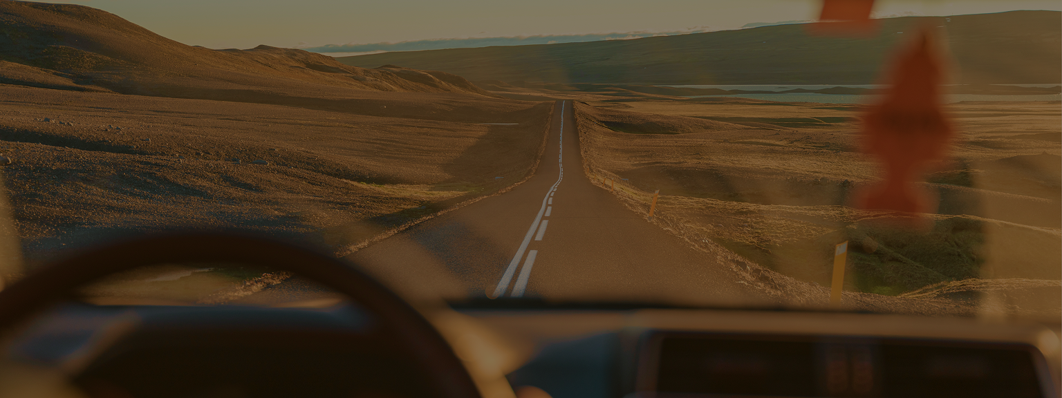View from the inside of a car windshield looking out towards a road cutting through fields.