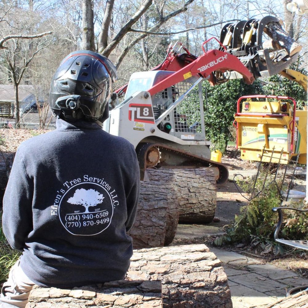 An Efren&rsquo;s Tree Services crew member monitors a residential job site as heavy machinery, including a skid steer and wood chipper, efficiently processes large logs and tree debris for cleanup.