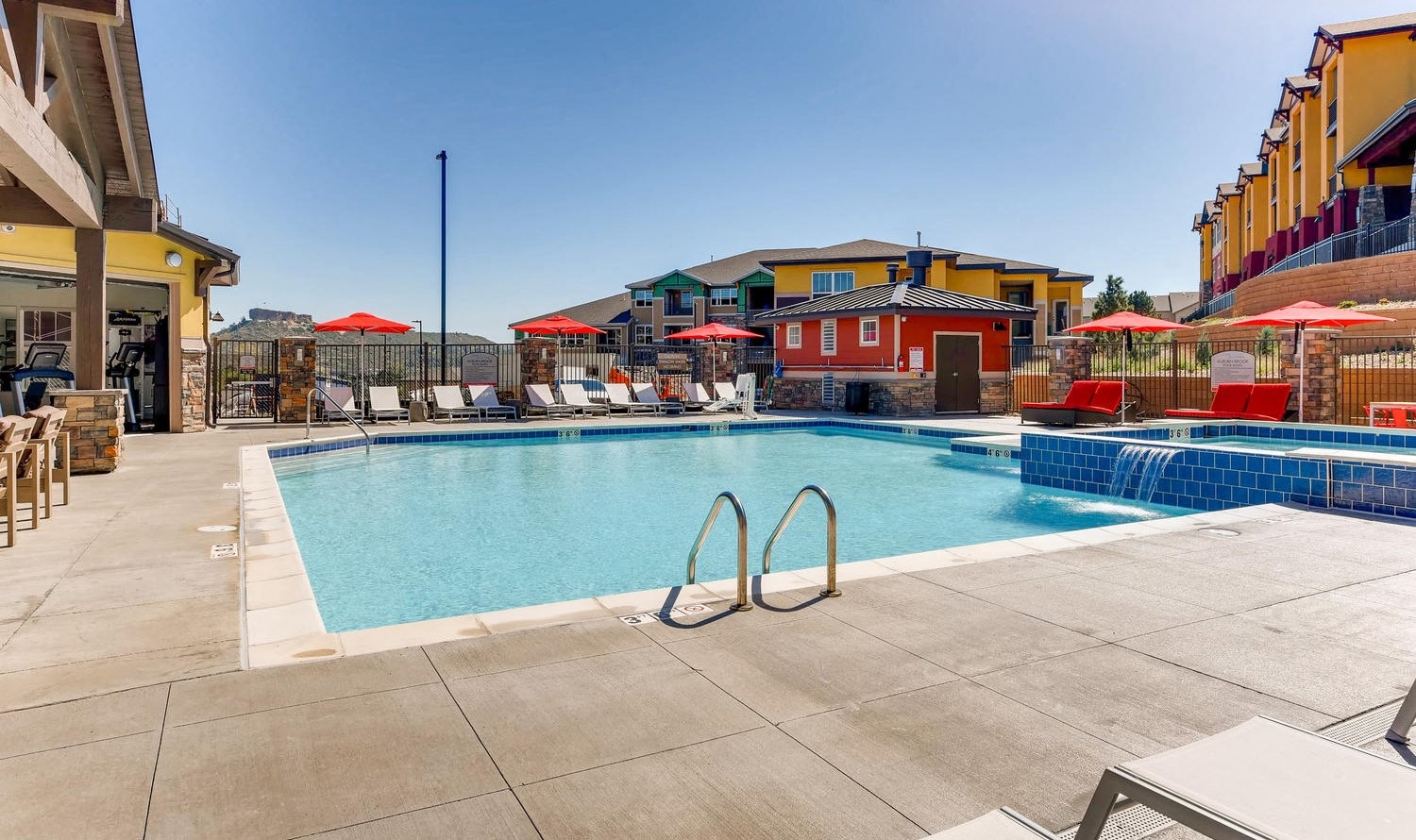 A swimming pool surrounded by a patio with chairs and umbrellas.