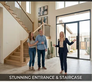 A woman in a navy blue suit is showing a couple a stunning entrance and staircase in a modern home. The entrance features a large glass door and window, with potted plants on either side. The staircase is made of wood with black metal railings. The walls are decorated with modern art.