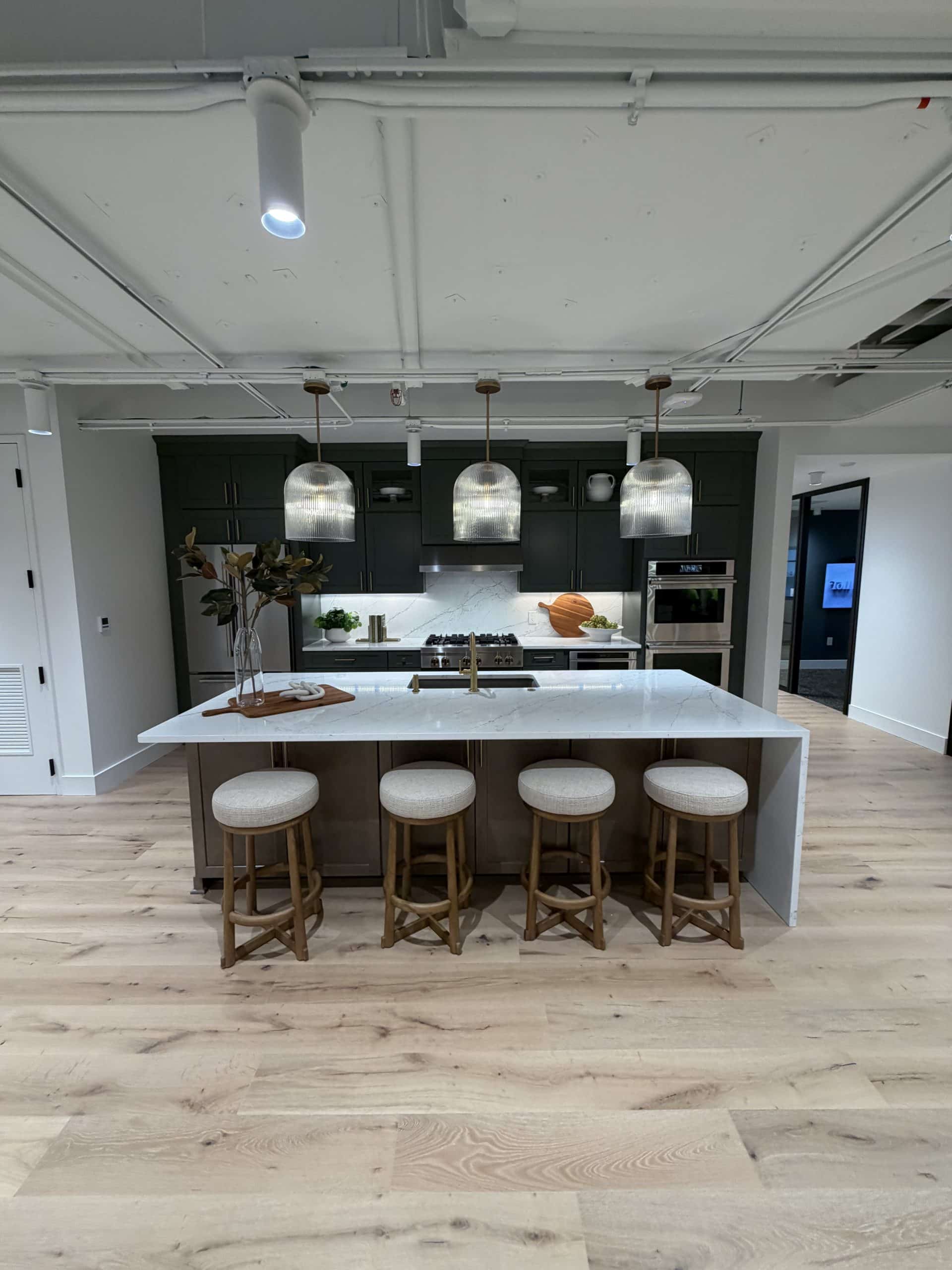 A kitchen display at the Toll Brothers Michigan Division Office & Design Studio highlights the distinctive showroom interiors within Schonsheck, Inc.’s commercial construction portfolio. Dark cabinetry, a spacious island, decorative pendant lighting, and stainless steel appliances create an inviting setting for exploring kitchen finishes and design possibilities. The space combines visual appeal with a practical layout, bringing the studio’s selections to life in a realistic kitchen setting.