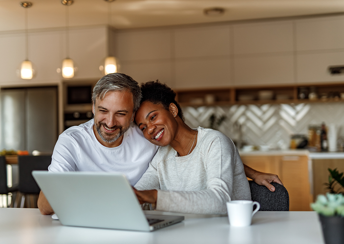 A couple sitting in the kitchen and looking at their laptop.
