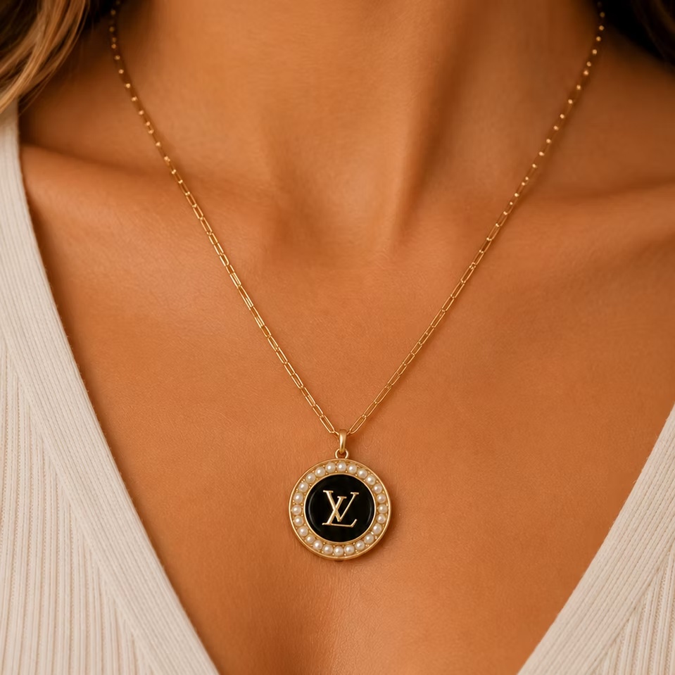 Close-up of The Pearl LV Medallion Necklace worn on a model, featuring a delicate gold chain and a circular pendant with a black enamel center, gold-tone logo, and a border of white pearls.