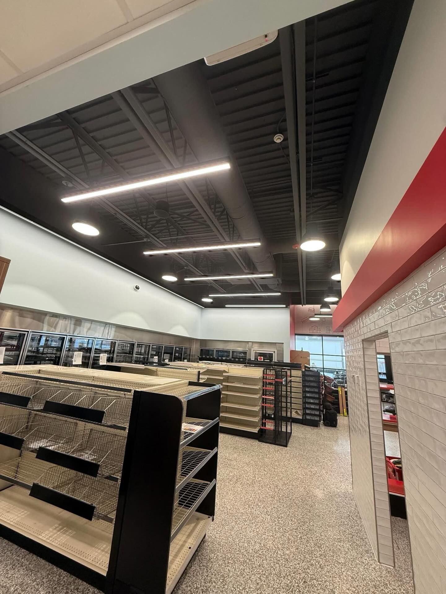 Retail store interior with shelving units, refrigeration cases, and modern lighting, showing nearly completed setup with organized aisles and clean design ready for stocking and customer access.