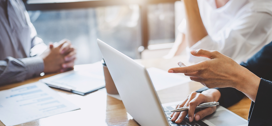 Close-up of three people sitting around a desk pointing at documents and a laptop.