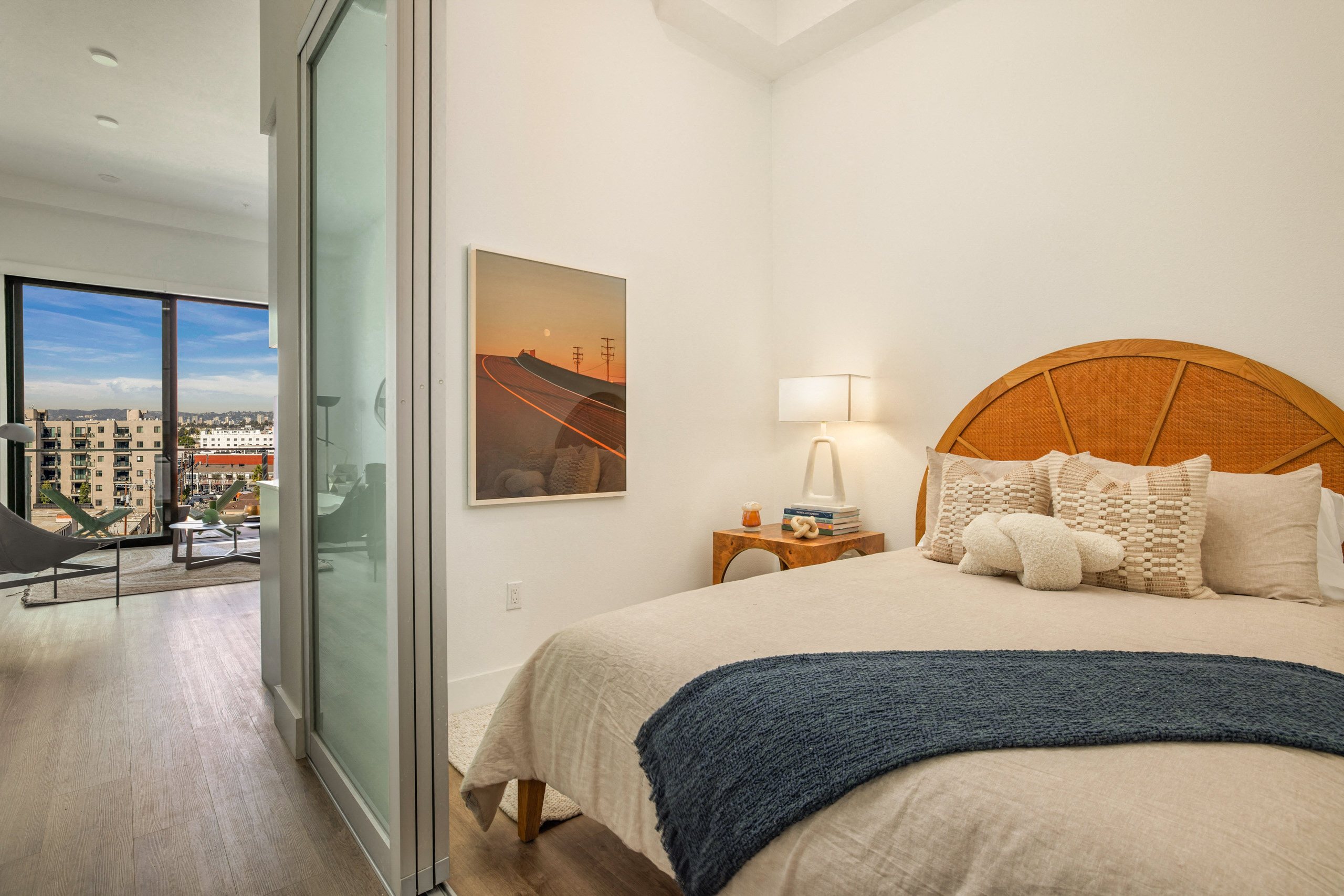 A bedroom with a large bed and a painting of a road with power lines on the wall.