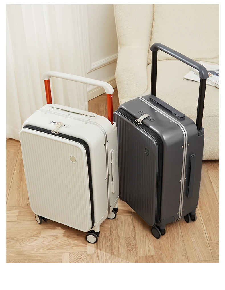 Two modern suitcases, one white and one dark gray, stand on a wooden floor next to a plush cream-colored armchair. The suitcases have textured surfaces, integrated TSA-approved locks, and telescopic handles. The white suitcase features orange accents on its handle, while the gray one has a sleek, unadorned handle. The scene is well-lit, highlighting the clean lines and contemporary design of the luggage.