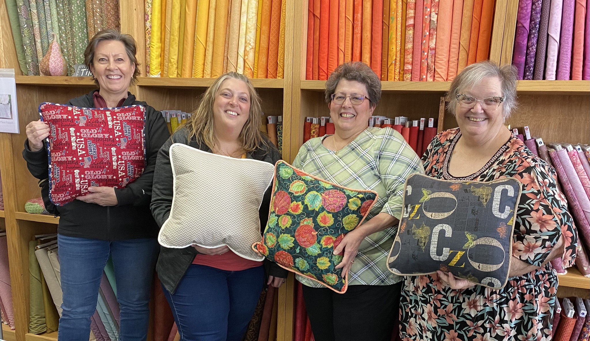 Students proudly showcase their finished custom throw pillows after a Decorative Stitch class. This hands-on sewing workshop featured decorative stitching, piping, construction techniques, and personalized home décor projects.