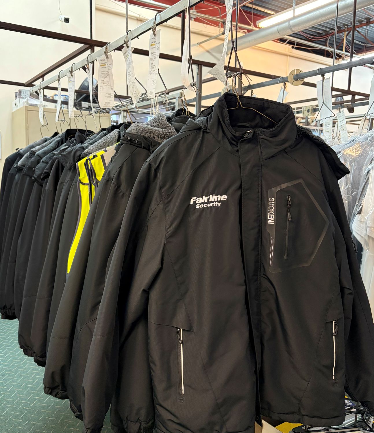 A rack of heavy-duty winter coats and branded security jackets hanging neatly after professional laundering and care at Plaza Cleaners.