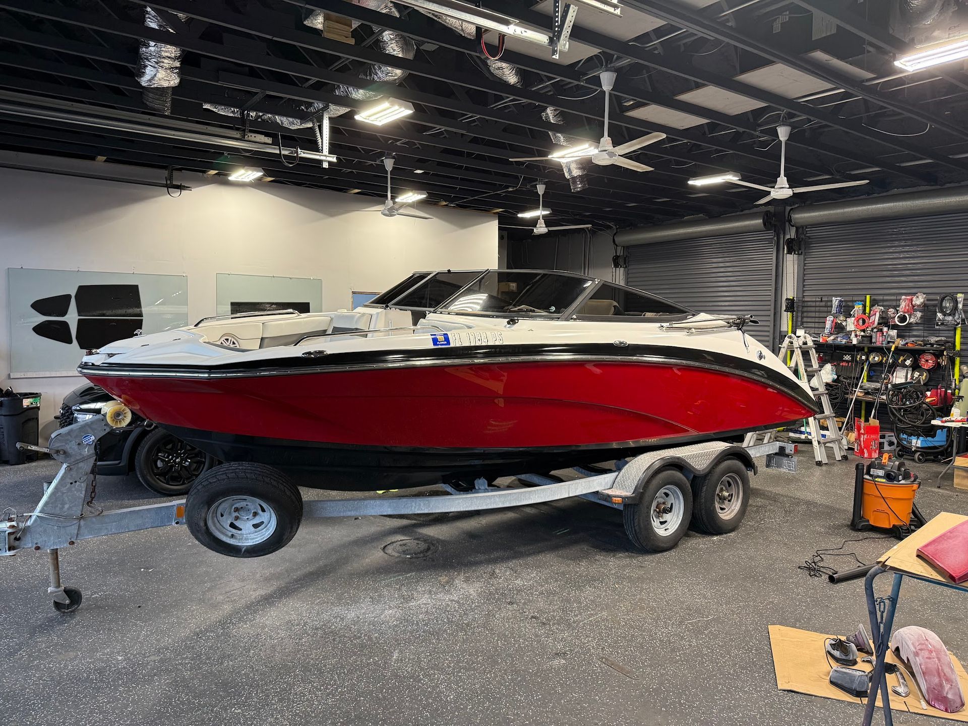 A sleek, red and white speed boat with a black accent stripe is fully staged on a dual-axle trailer inside a brightly lit, modern garage bay, ready for service or detailing.