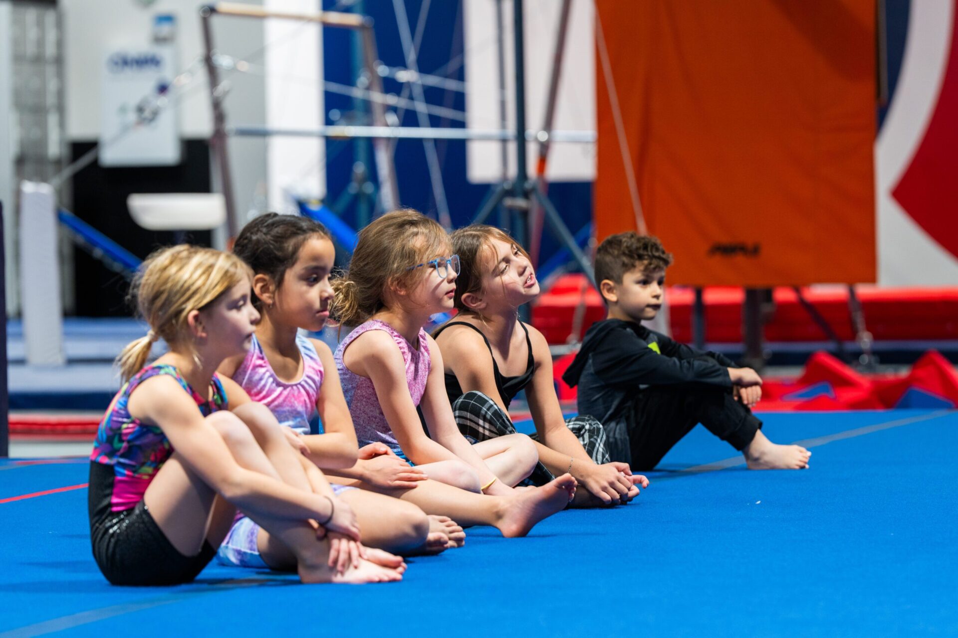 A group of young children sitting and listening intently to their gymnastics coach