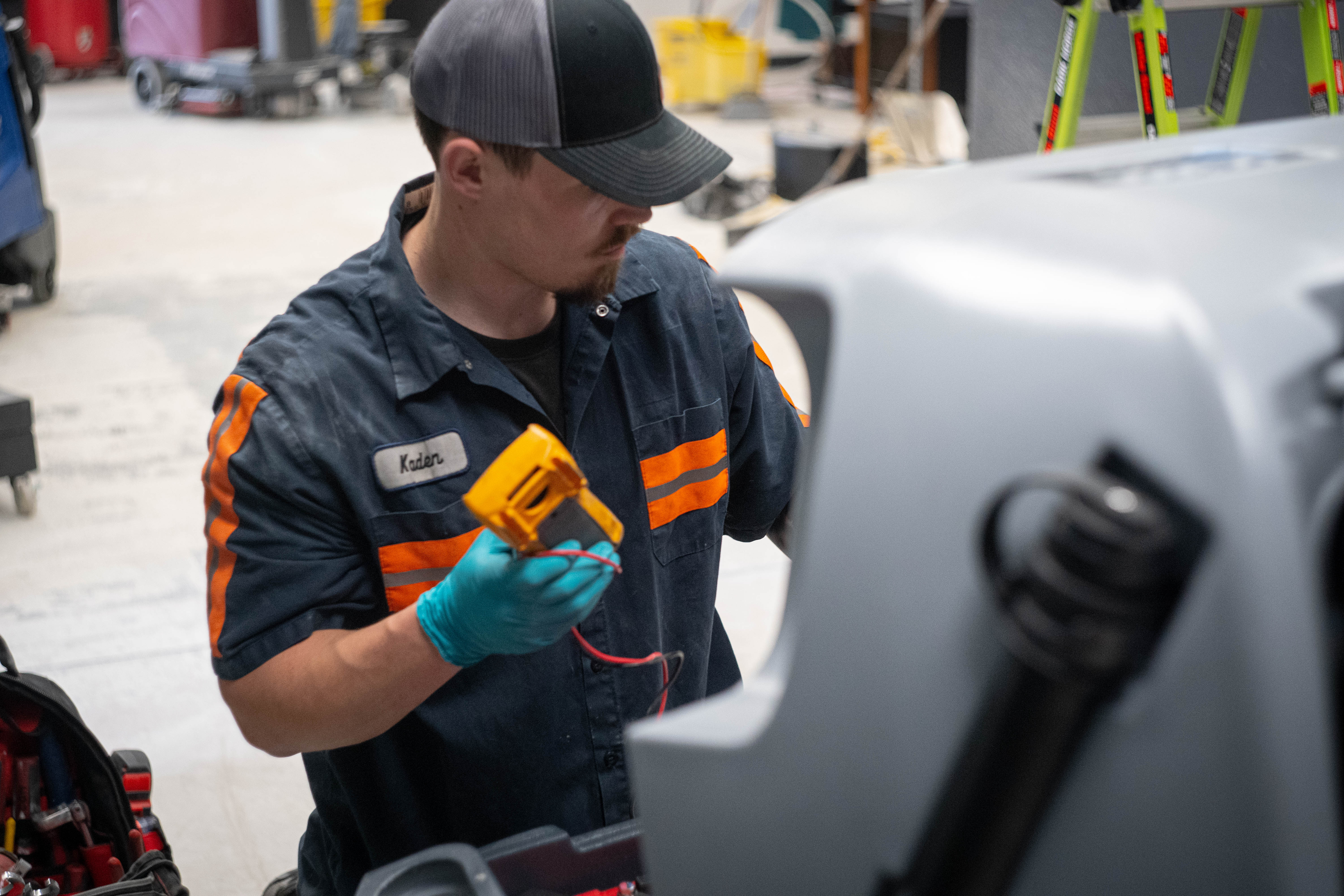WaySolutions lead technician Kaden uses a yellow digital multimeter to perform precision electrical diagnostics on a commercial floor scrubber. Our Layton-based repair team expertly traces complex wiring faults to ensure reliable, uninterrupted performance for your heavy-duty cleaning equipment.