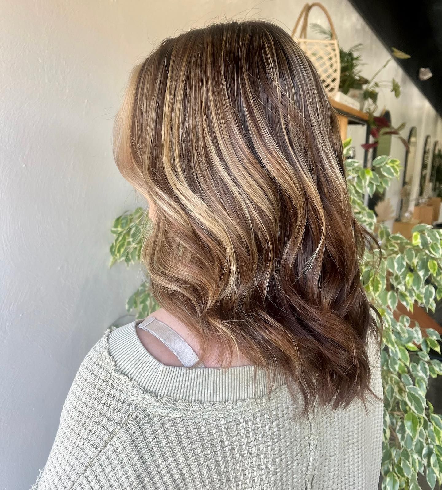 Side back view of medium-length brown hair with blonde highlights, styled in soft waves creating a natural dimensional salon look.