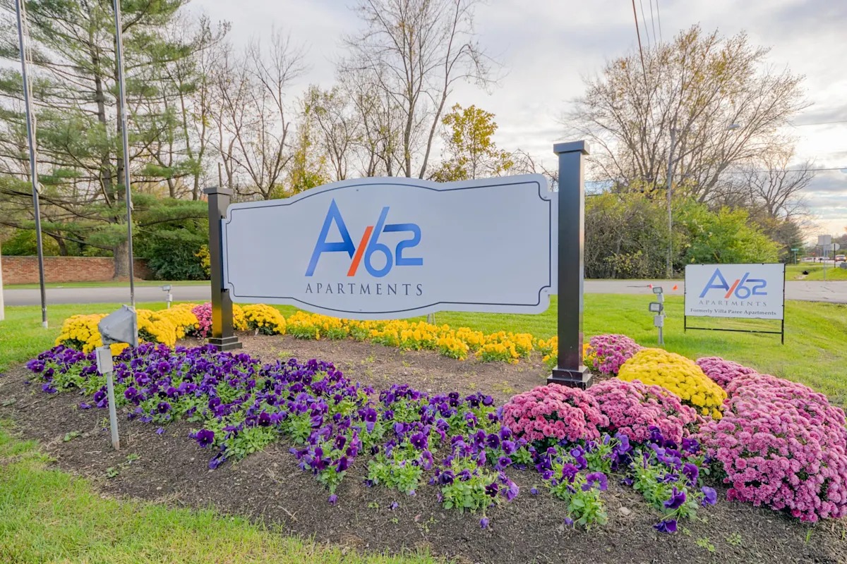 A sign for A/62 Apartments is surrounded by flowers