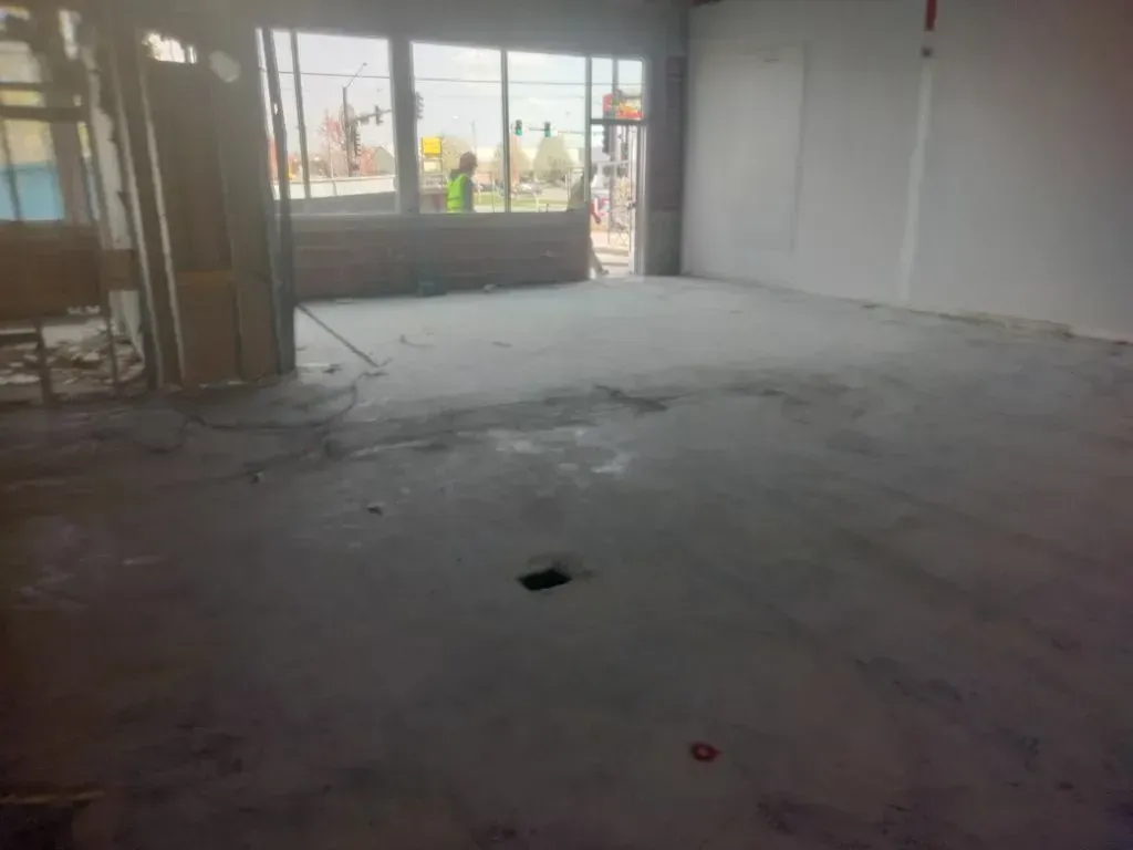 Empty commercial interior space after demolition, with cleared floor, exposed areas, and minimal deb 