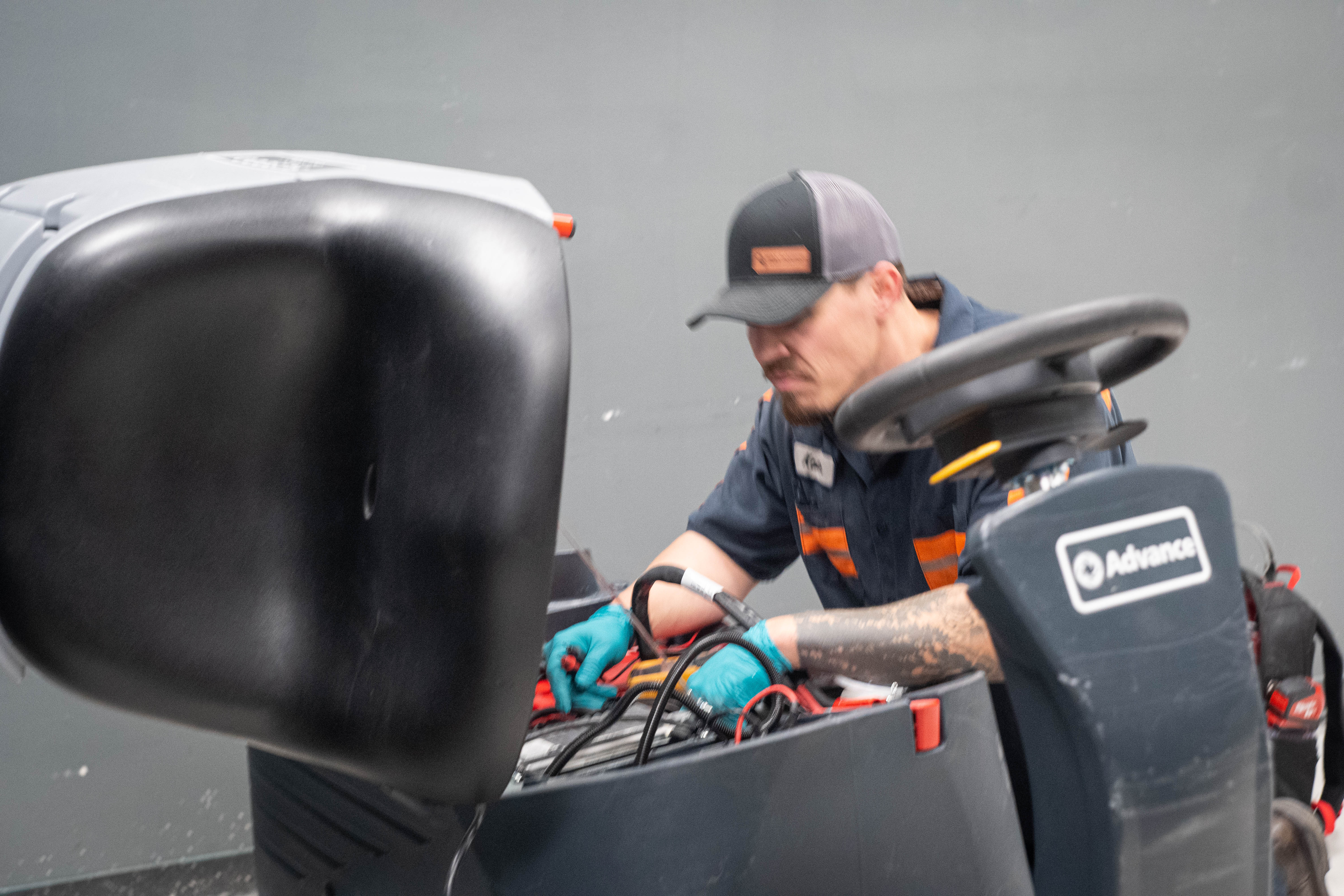 A WaySolutions field technician performs deep electrical wiring inspections under the hood of a heavy-duty Advance ride-on commercial floor scrubber. Providing expert fleet maintenance in Layton, Utah, our team traces complex wiring harnesses to prevent unexpected power loss during critical cleaning shifts.