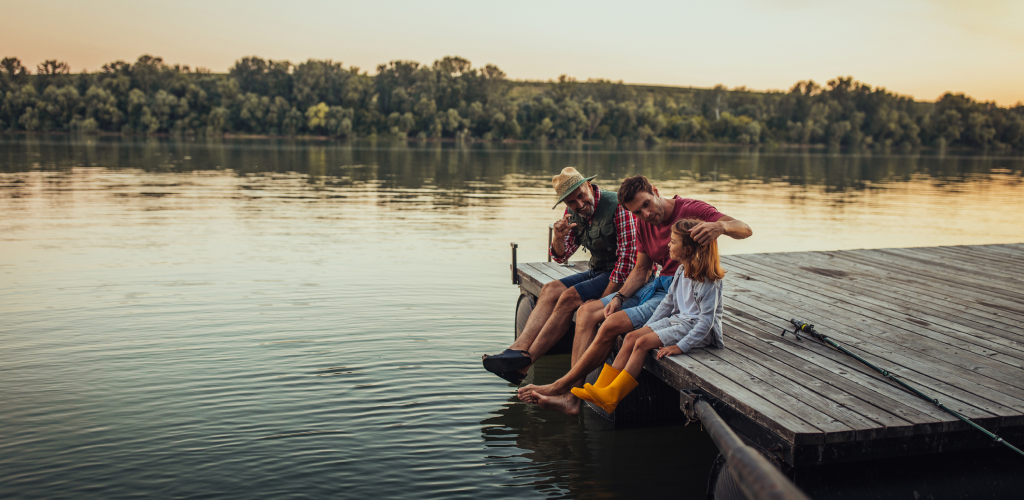 A grandfather with his son and his grandchild sitting on a dock together.