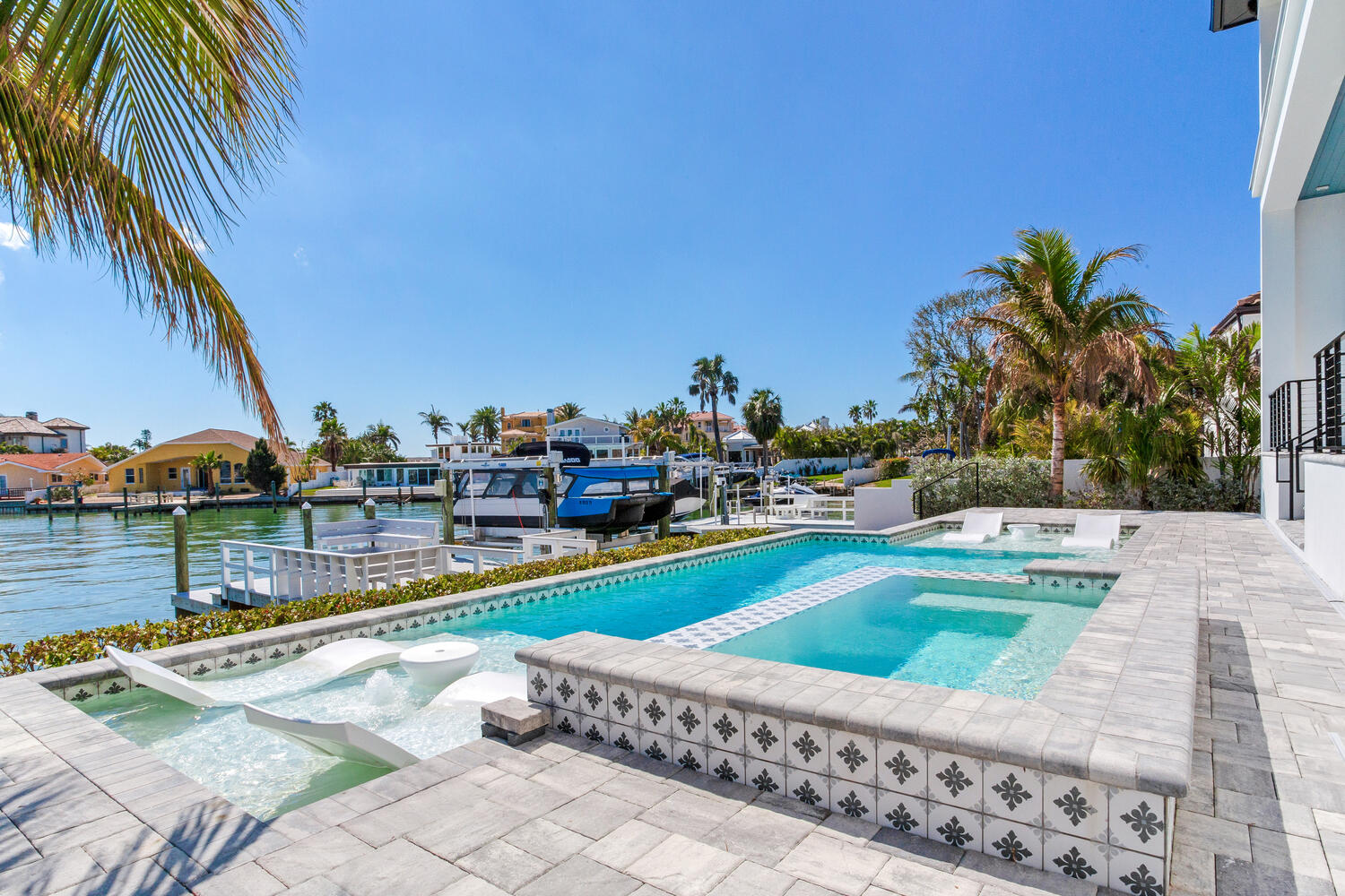 Luxury waterfront backyard with a swimming pool, spa, paver patio, palm trees, and scenic canal views.