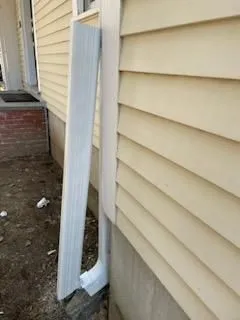 Newly installed white downspout attached to beige vinyl siding. Downspout efficiently channels rainw 