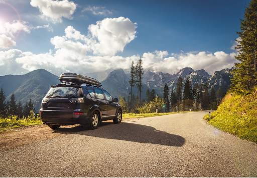 An SUV parked on the side of a road with a scenic mountain range in the background.
