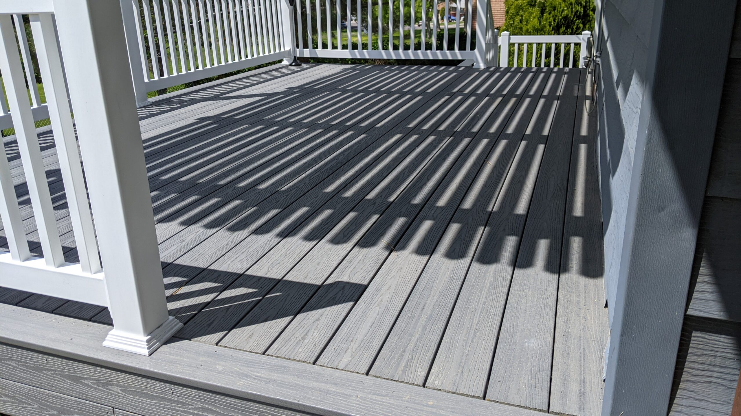 Extend your upper-level living space with this cozy raised composite deck by DeckPro LLC, designed for tranquility and function. We installed low-maintenance composite decking in a warm brown tone and a matching perimeter railing system. Furnished with a comfortable dark Adirondack chair, it's the perfect retreat to take in the serene views of the surrounding pine trees and rustic outdoor setting.