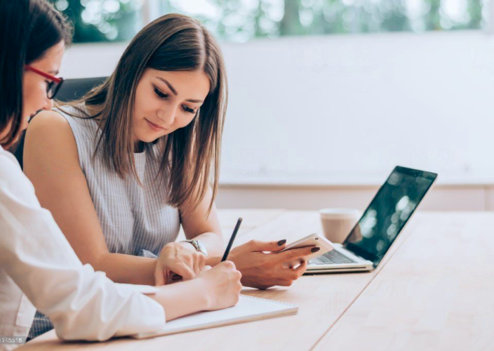 Two women working beside each other at a desk.