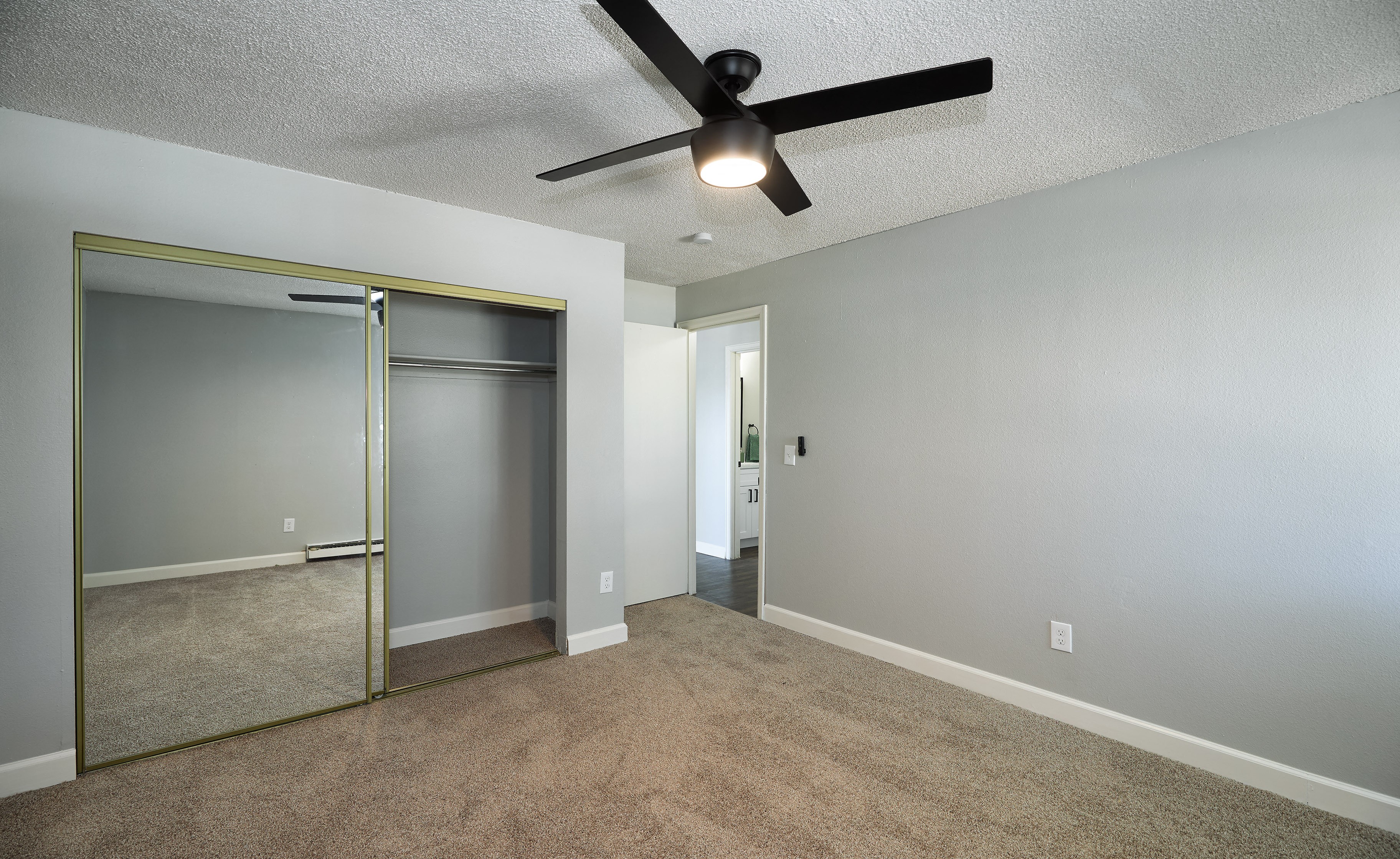 an empty living room with a ceiling fan and a mirrored closet 