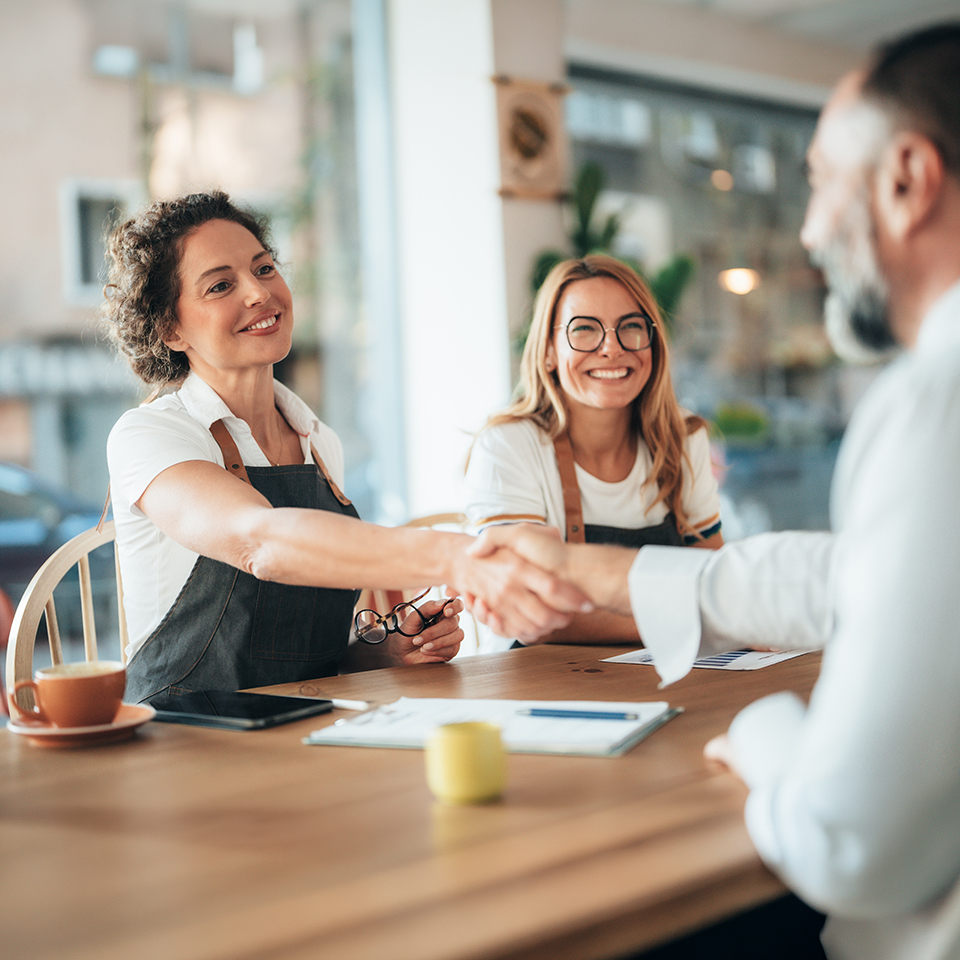 A woman in an apron shaking hands with a man an another woman is nearby in an apron.