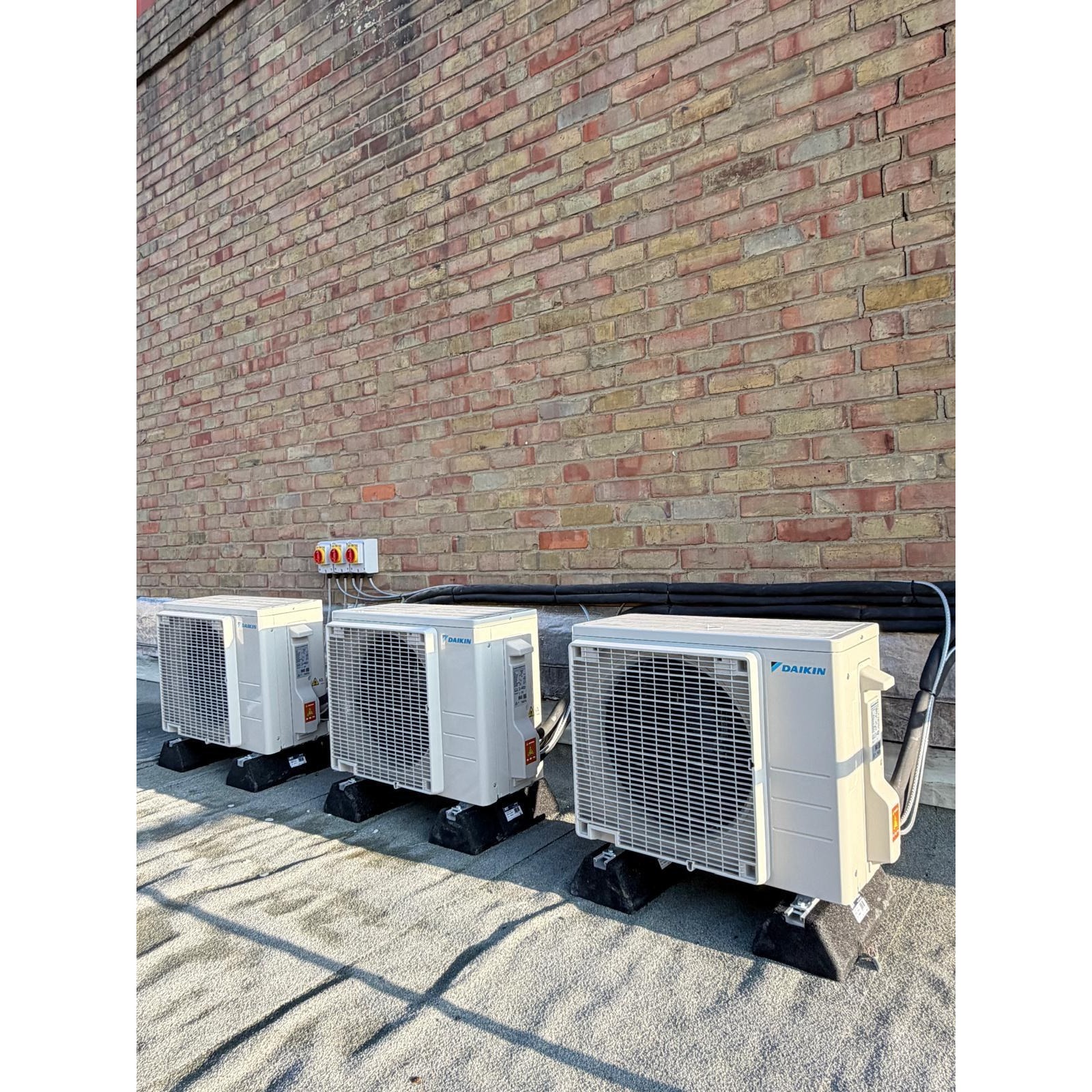 Three Daikin outdoor units installed on a London rooftop, raised on feet with tidy pipework.