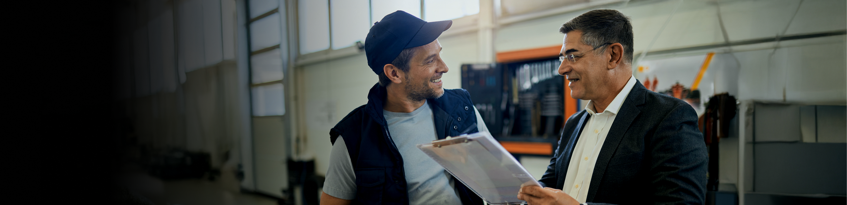 Two workers talking over a clipboard in a service garage.