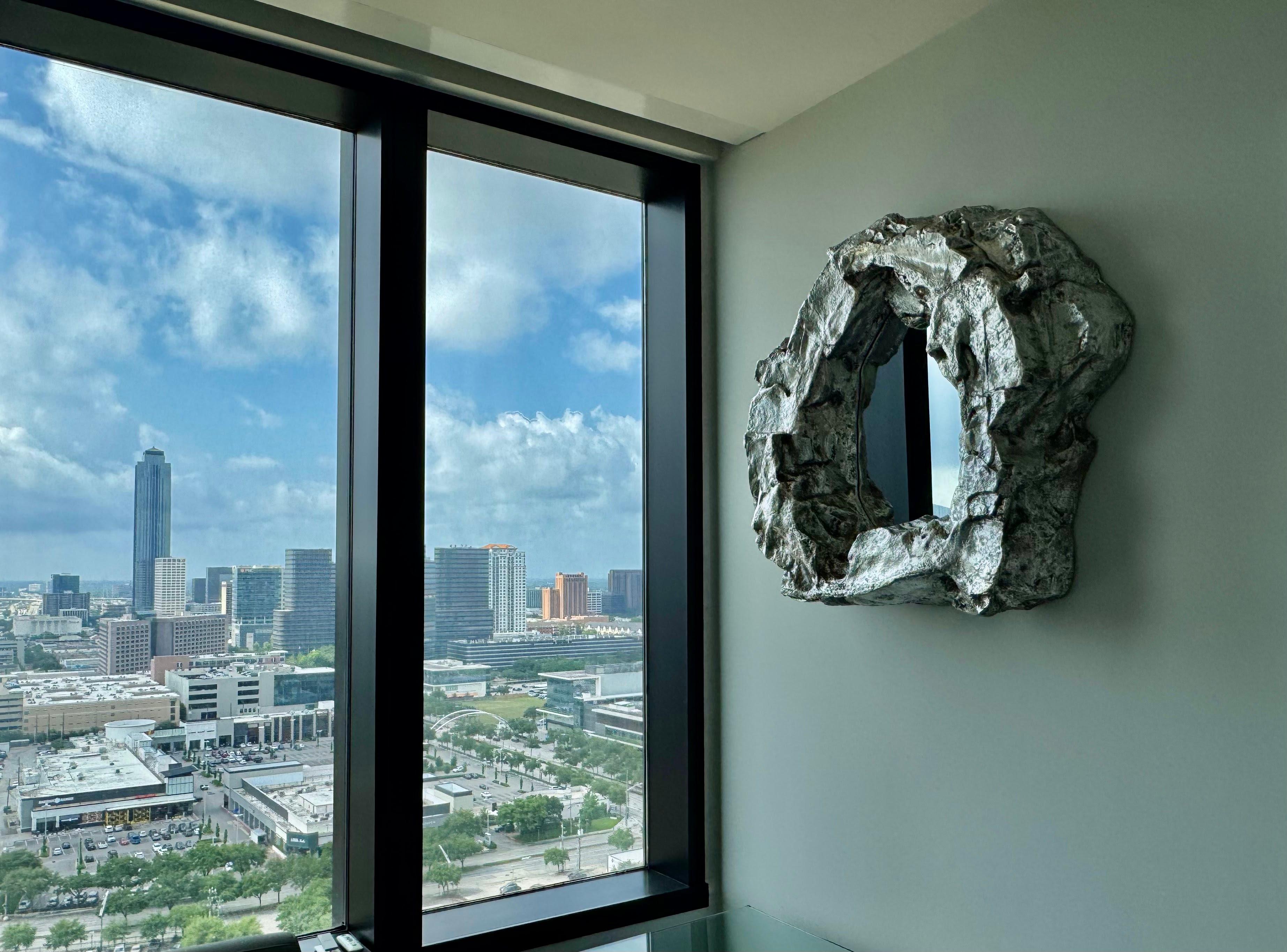 Lava rock style wall mirror installed beside large windows in a Houston high-rise residence.
