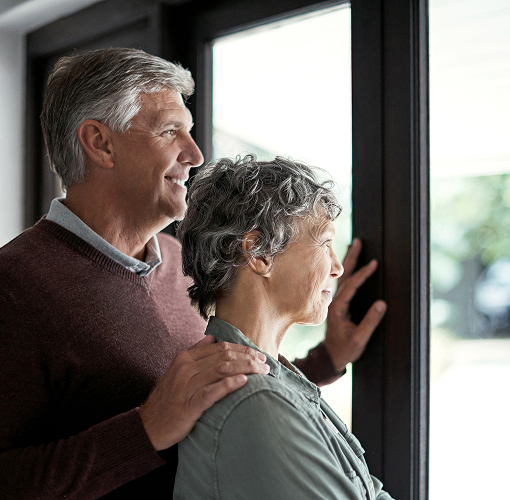 A husband and wife looking out of a window together.