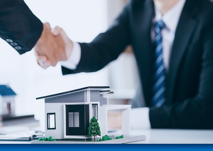 Close up of two professionals shaking hands behind a scaled-down model home.