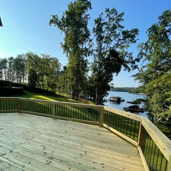 Spacious wooden deck overlooking grassy yard, trees, and calm lake view.