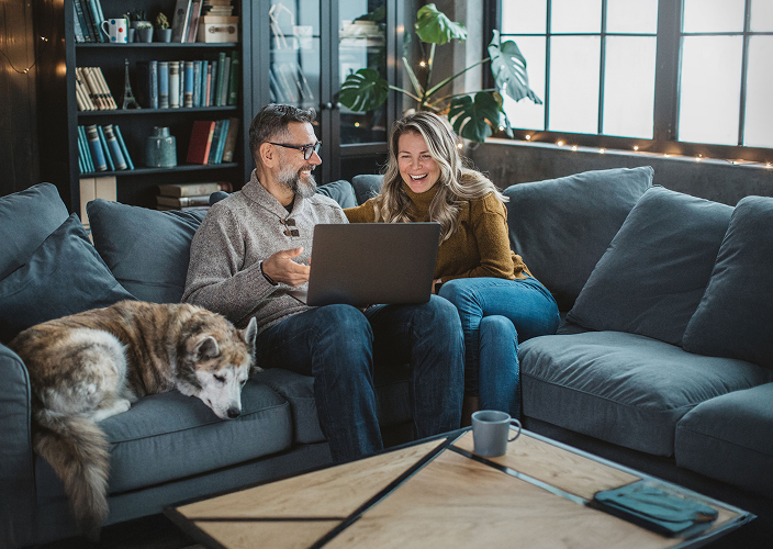 Two people and a dog looking at a laptop on a couch.