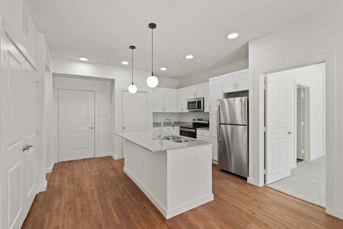 A kitchen with white cabinets and a wooden floor. 