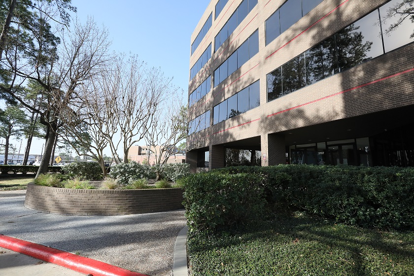 The photo of the entrance of the building of our Houston office showcases a modern and sleek design that exudes professionalism and sophistication. The entrance is framed by a large glass door that provides a glimpse into the welcoming and inviting lobby. The photo captures the surrounding landscape, which is well-manicured and adds to the overall aesthetic appeal of the building.