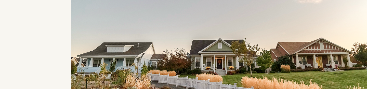 Two well-maintained detached family homes and their shared front lawn surrounded by a white picket fence.