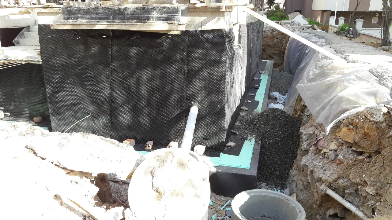 Exterior foundation waterproofing project showing protective membrane application around building foundation. Excavation exposes walls for waterproofing, drainage enhancement, and long-lasting protection against groundwater infiltration and moisture damage.