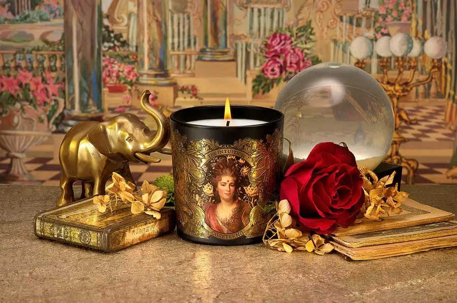 A captivating product visual generated by Tabula Rasa Social Stationers, highlighting a Coreterno "The Intuition" scented candle. The candle's black vessel, richly embellished with intricate gold detailing and a classical portrait, epitomizes the brand's luxurious and rebellious design ethos. Arranged with a golden elephant figurine, a vibrant red rose, and antique books, the image evokes a sanctuary of style and mystery, reflecting Coreterno's commitment to storytelling through exquisite scents and symbolic artwork.