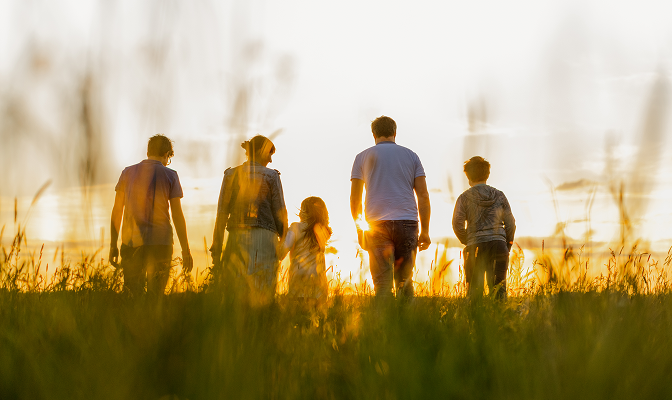 A multigenerational family standing in a field at sunset.