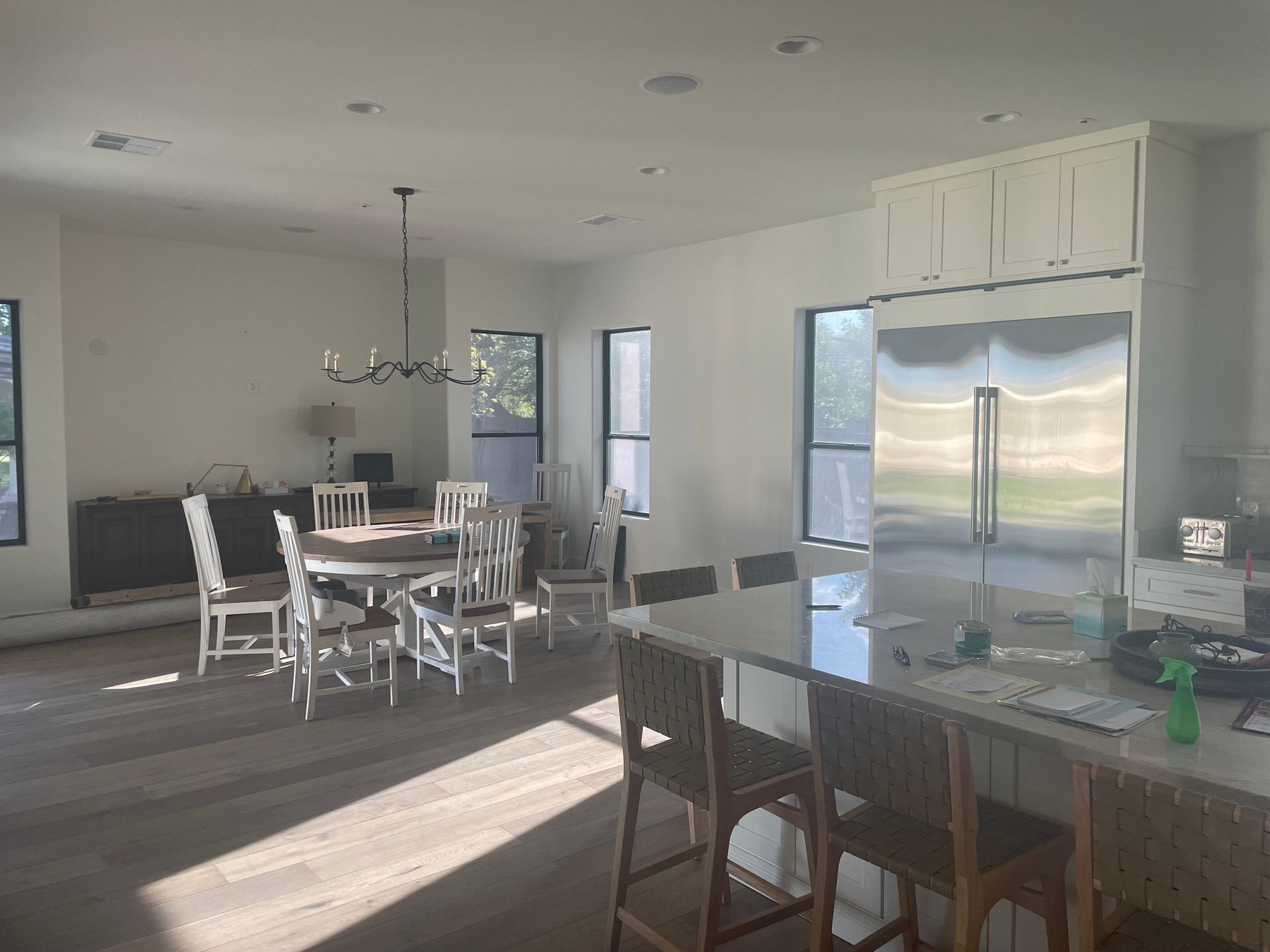 A spacious open-concept kitchen and dining area with a large island, bar seating, stainless steel refrigerator, wooden dining table, and abundant natural light creating a bright, modern interior environment.