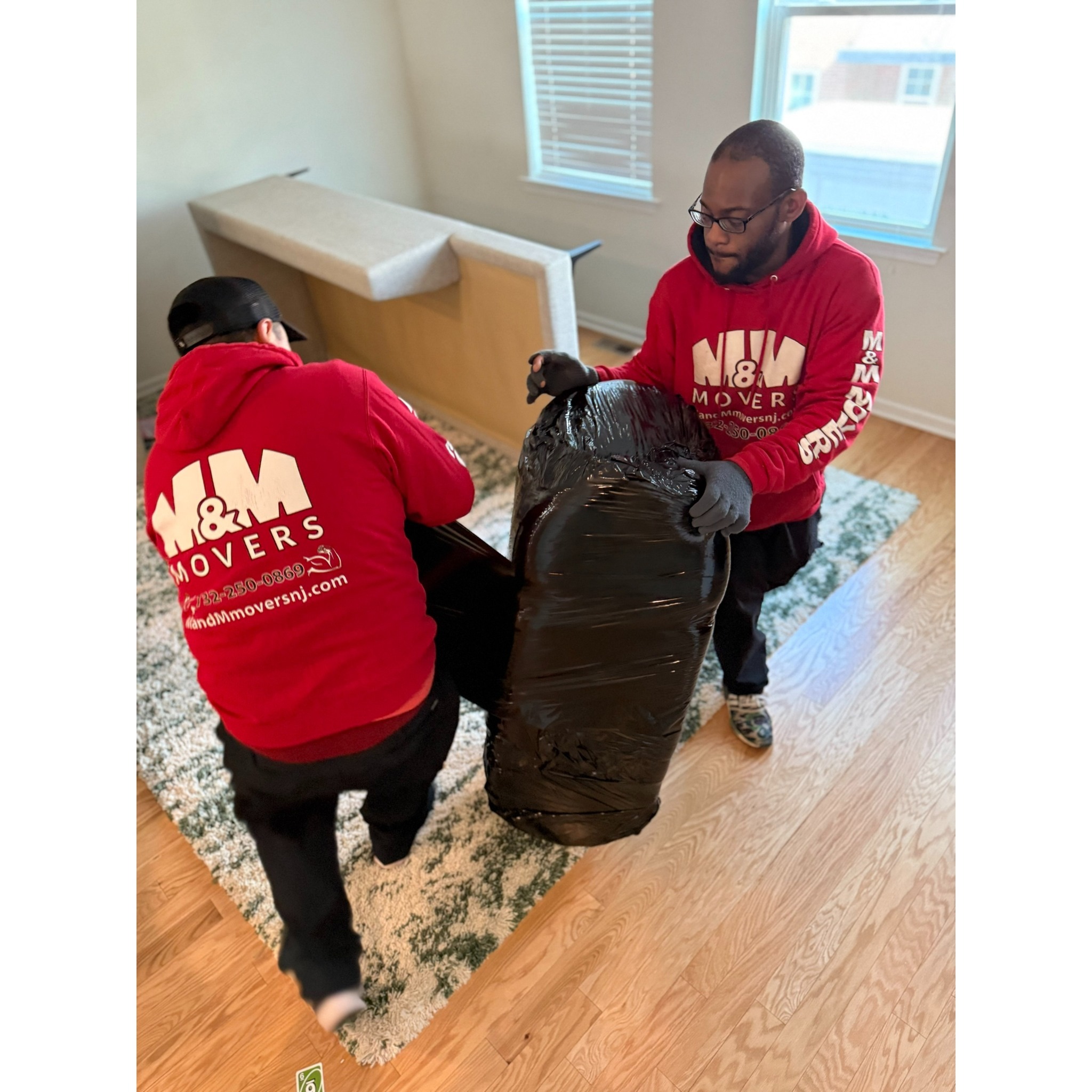 M&M Movers crew carefully shrink-wrapping and securing a large chair/sofa piece inside a home to protect it during transport.