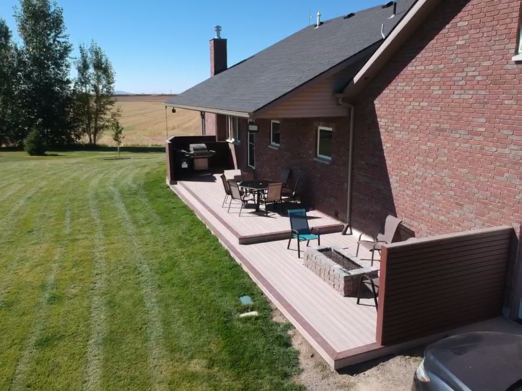Transform your outdoor living space with a custom ground-level composite deck from DeckPro LLC. This expansive project features light brown composite decking that spans the length of the home, a built-in fire pit for cozy gatherings, and a stylish dark brown privacy wall to create a secluded retreat. It's the perfect blend of function and modern design.