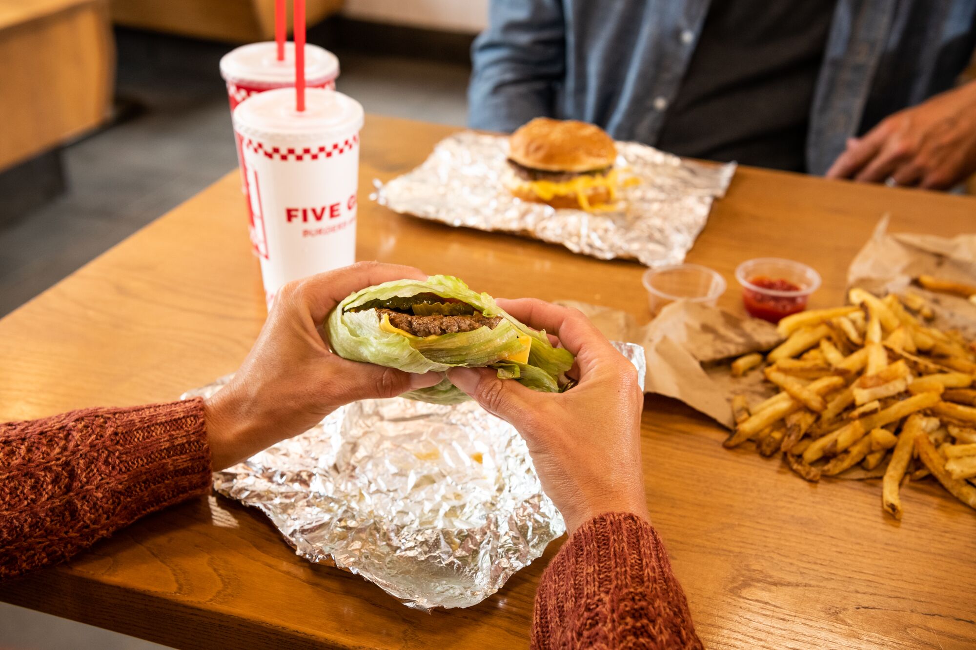 A customer's hands hold a Five Guys lettuce wrap at a dining room table inside a Five Guys restauran Five Guys Thousand Oaks (805)496-0173