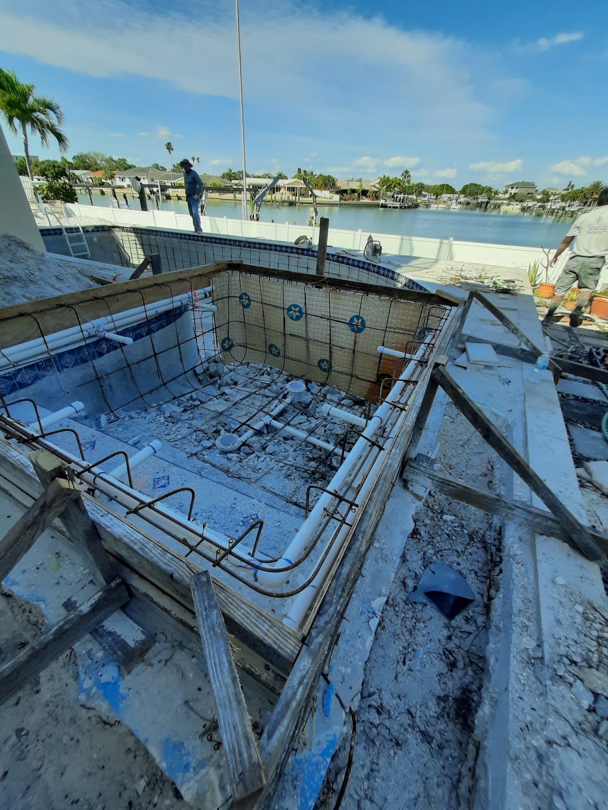 Waterfront swimming pool under construction with exposed steel reinforcement, concrete framing, and scenic water views.