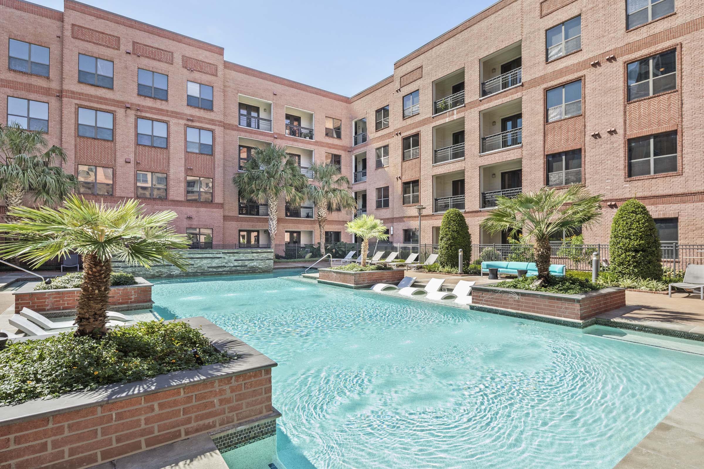 Resort style pool with greenery surround and in the water sun loungers at Camden Travis Street Apartments in Midtown Houston, Tx